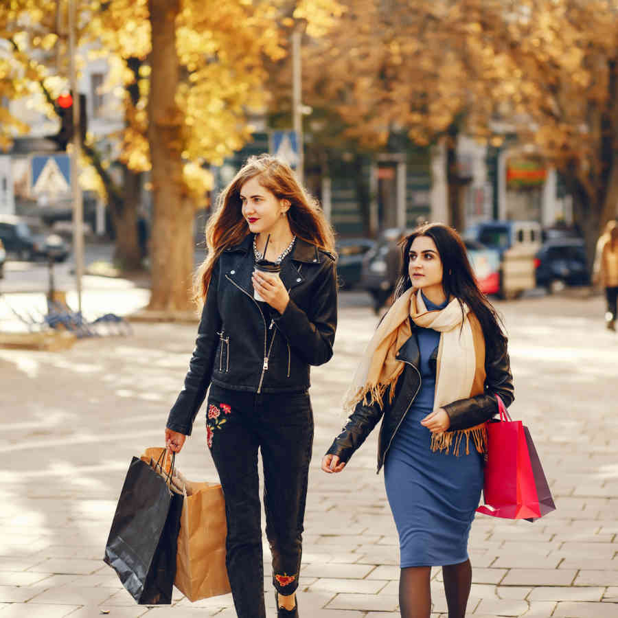 Two beautiful elegant girls walking around city with shopping bags