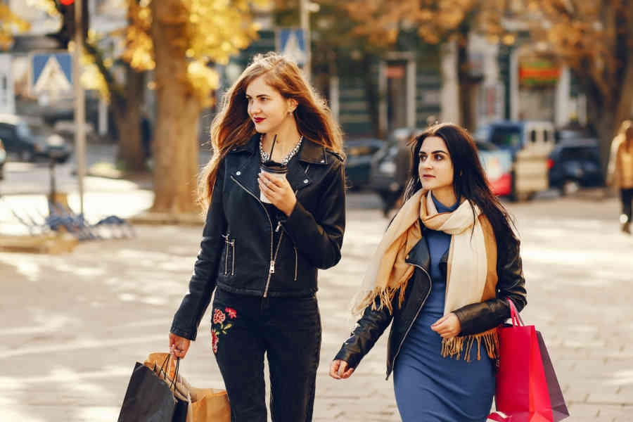 Two beautiful elegant girls walking around city with shopping bags